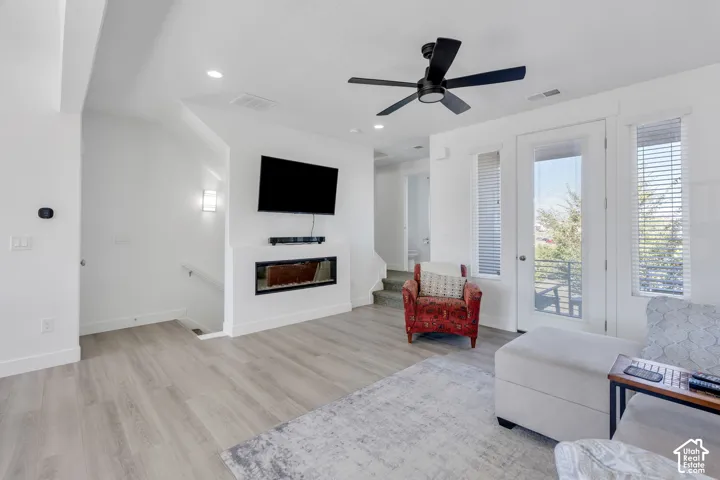 Modern living area with wood-finish flooring, a built-in electric fireplace, and a contemporary black ceiling fan