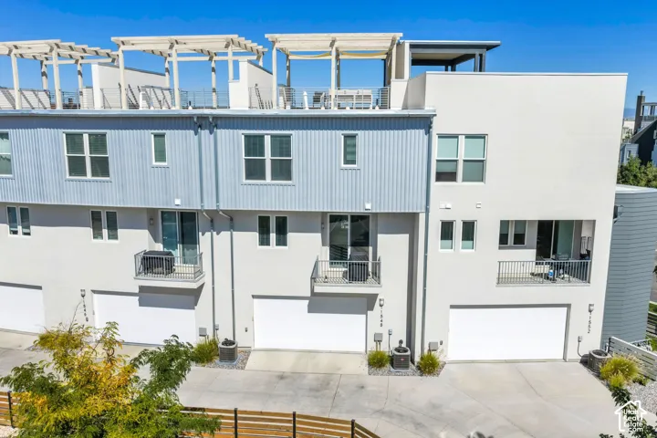 Modern townhouse exterior featuring multiple balconies with metal railings, a rooftop patio with pergolas, and integrated garage doors