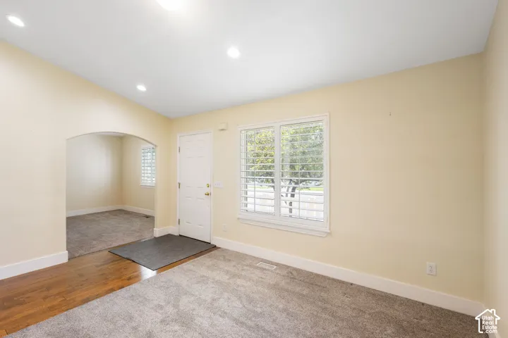 Recessed lighting, arched doorway, wood-finish flooring, white window shutters, and a white entry door