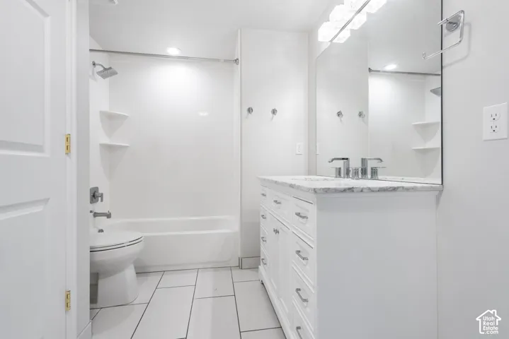 White tile flooring, white vanity with a stone countertop, built-in tub and shower combination, and a large wall-mounted mirror