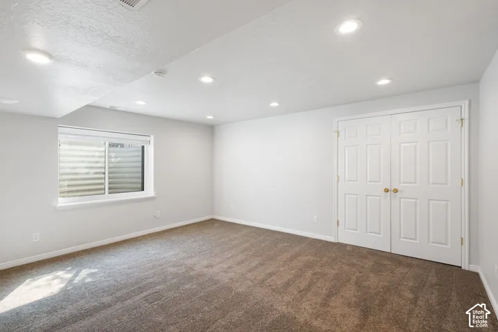 Recessed lighting, light gray painted walls, window with horizontal blinds, carpeted flooring, and white paneled bi-fold doors