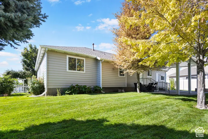 Rear exterior with light gray siding, white trim windows, a covered patio structure, and a green lawn
