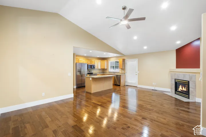 Vaulted ceiling with a ceiling fan and recessed lighting, wood-finish flooring, and a fireplace with a tile surround