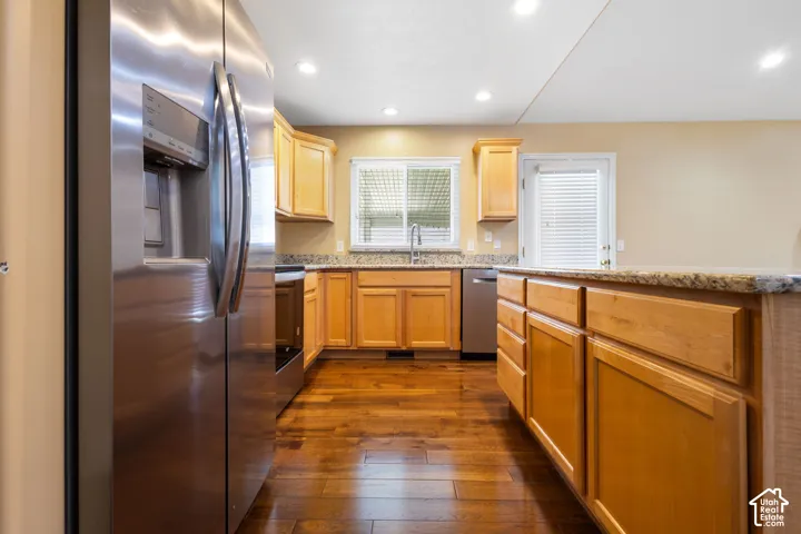 Kitchen featuring wood-finish flooring, stainless steel appliances, granite countertops, wood cabinetry, and recessed lighting