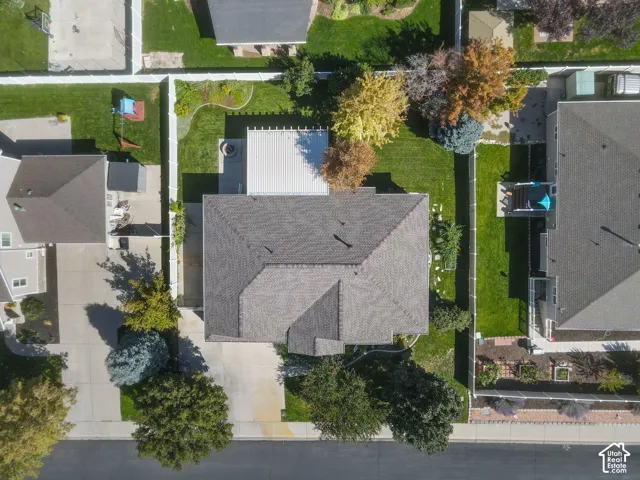 Expansive property featuring a paved driveway, a shingled roof, a well-maintained lawn, and mature trees