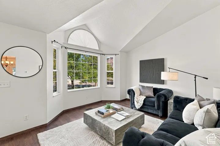 Vaulted ceilings with an arched window, rich wood-finish flooring, and a bay window