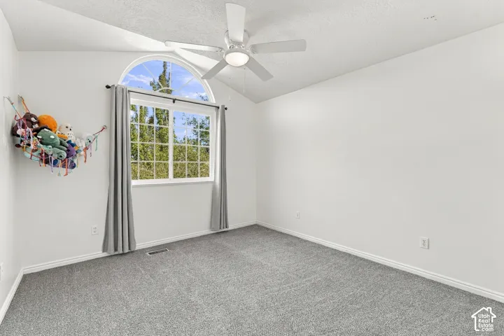 Vaulted ceiling with an attached ceiling fan, arched window, and gray carpeting