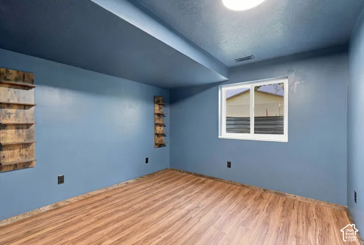 Wood-finish flooring with a window, ceiling light fixture, and built-in wall shelving
