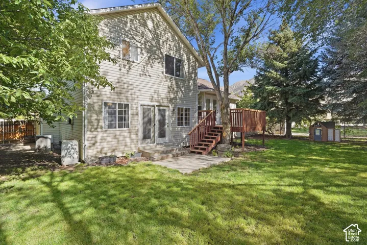 Two-story siding exterior with multiple windows, a rear deck with staircase, and a stone patio