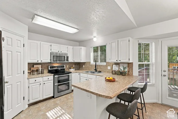 White cabinetry, stainless steel appliances, stone-finish countertops, tile flooring, and a built-in breakfast bar