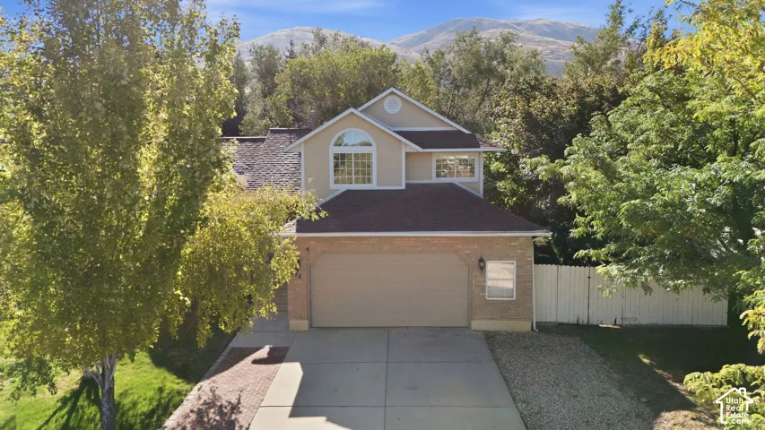 Two-story residential exterior with a front-facing garage, arched window, and mountain backdrop