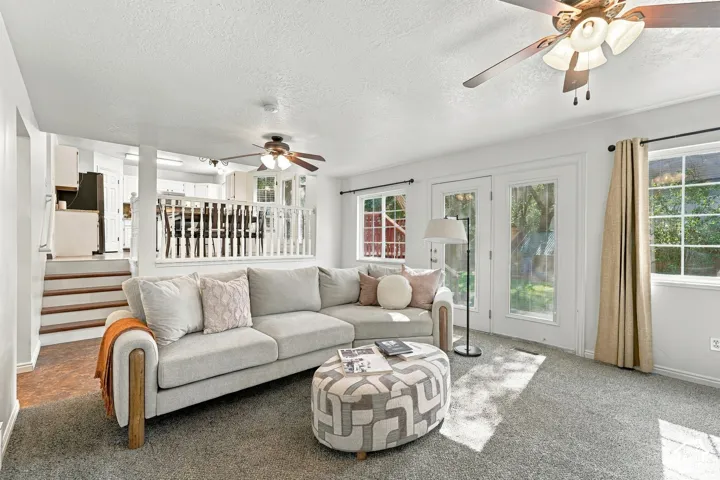 Carpeted living area with two ceiling fans, white walls, and wood-finish stairs