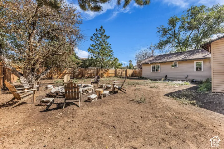 Fenced backyard featuring a fire pit area, mature trees, and a neutral-toned exterior siding
