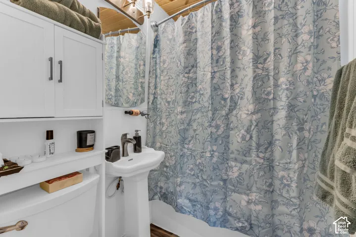 Pedestal sink with dark-toned faucet, white wall-mounted cabinetry, and wood-finish ceiling