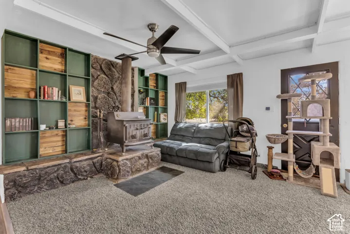 Stone-clad wood-burning stove with hearth, built-in shelving, exposed beam ceiling, and ceiling fan