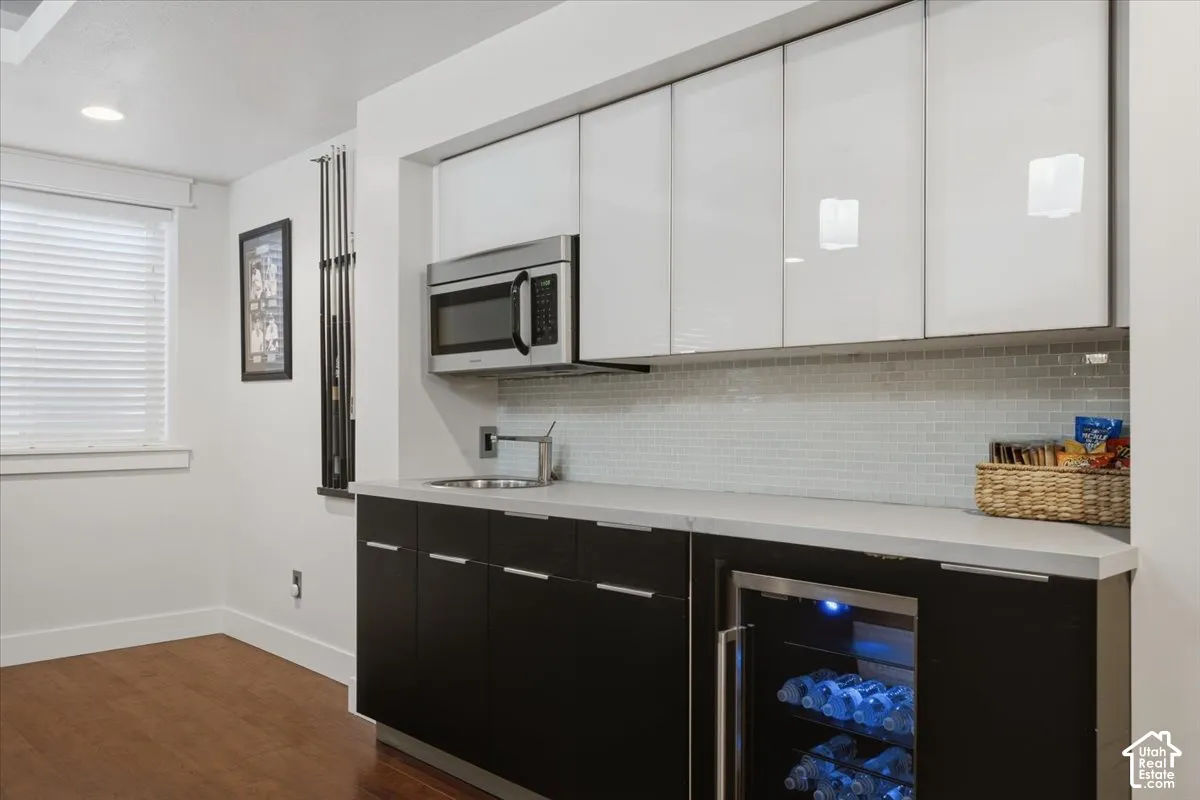 Wet bar with stainless steel microwave, integrated beverage cooler, undermount sink, and light gray backsplash