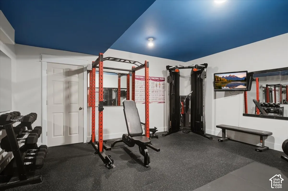 Dedicated fitness space featuring rubber flooring, a blue ceiling, wall-mounted mirrors, and an attached television