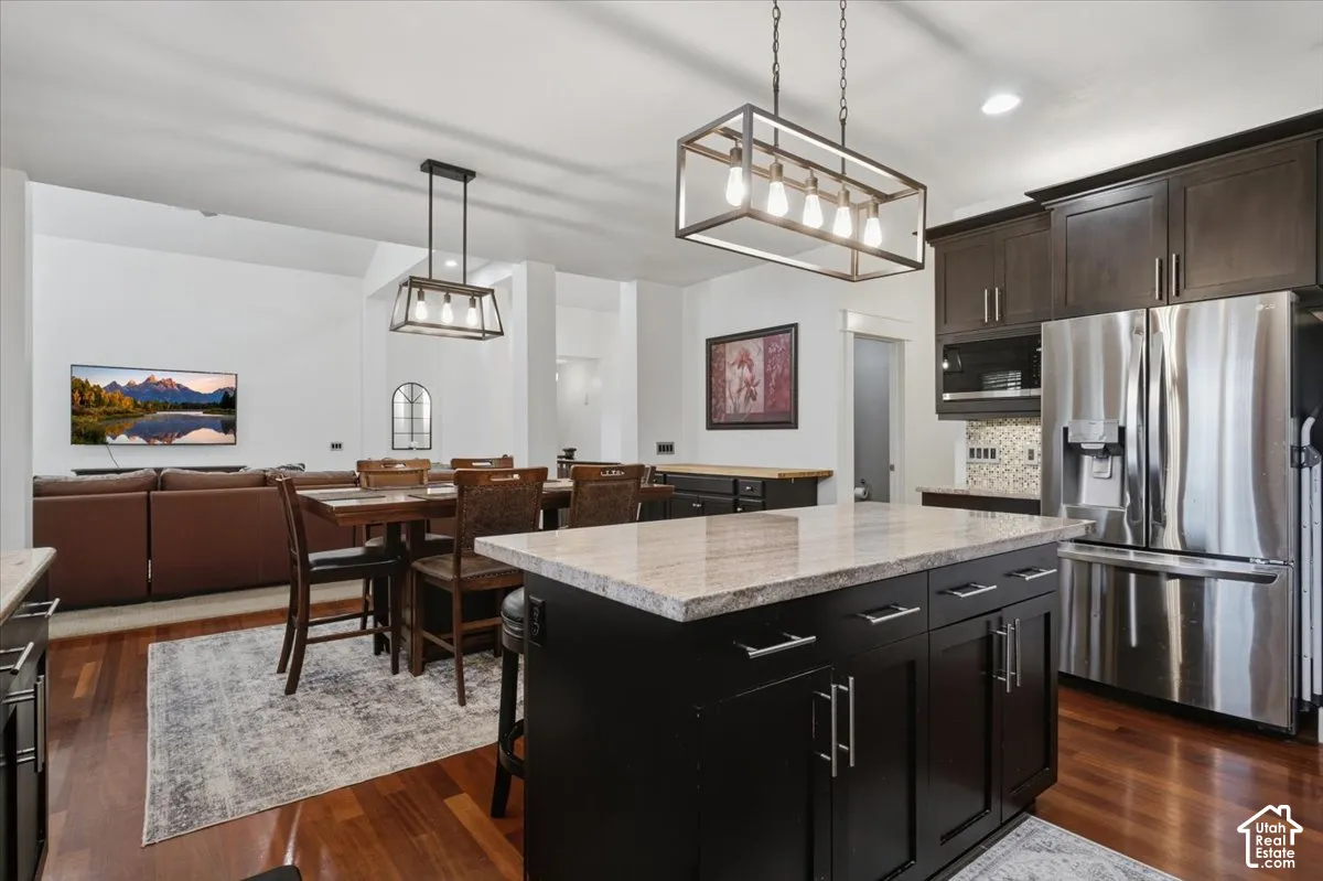 Hardwood flooring throughout, a kitchen island with stone finish countertop, dark wood-finish cabinetry, and stainless steel appliances