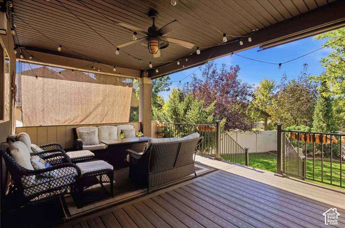 Covered deck with a ceiling fan, string lighting, and wood-finish flooring