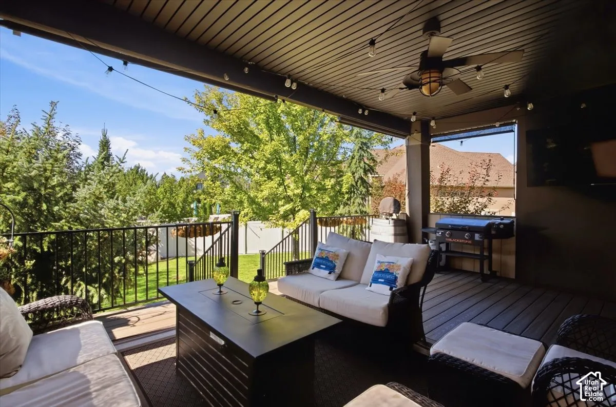 Covered outdoor living area featuring a ceiling fan, string lighting, and a dark wood-finish deck