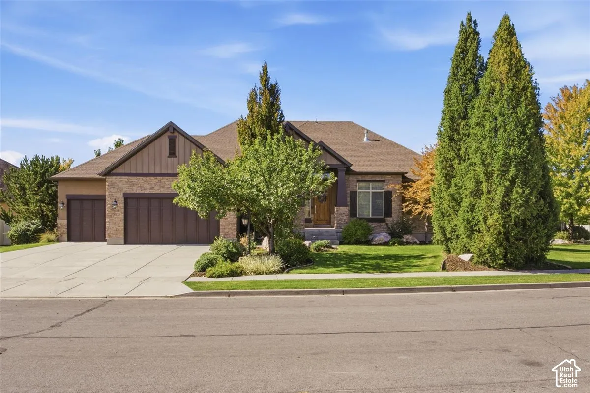 Stone and siding exterior with a multi-car garage, mature landscaping, and a well-maintained lawn
