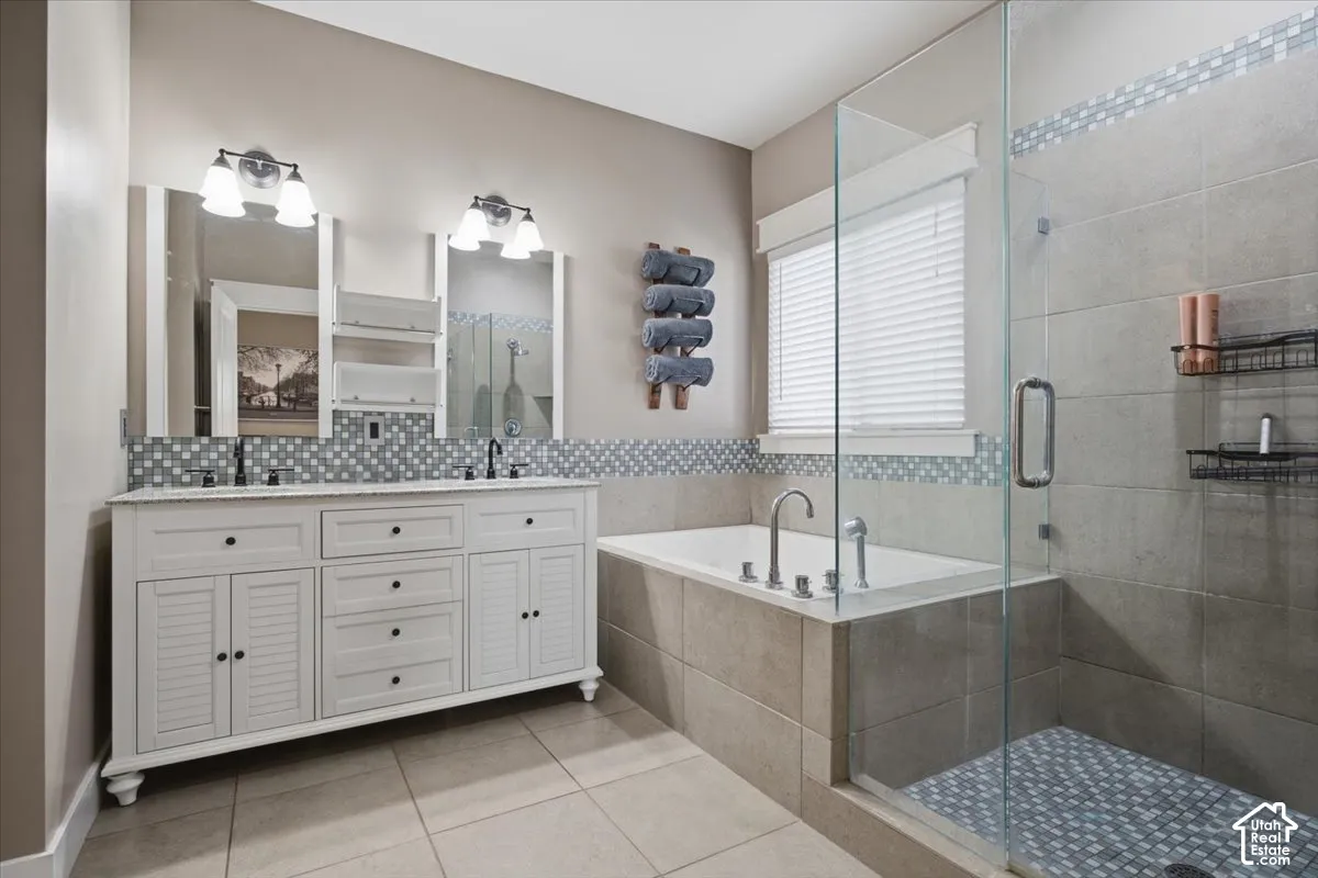 Dual vanity with white cabinetry, a built-in tub, a glass-enclosed shower, tile flooring, and a window with blinds