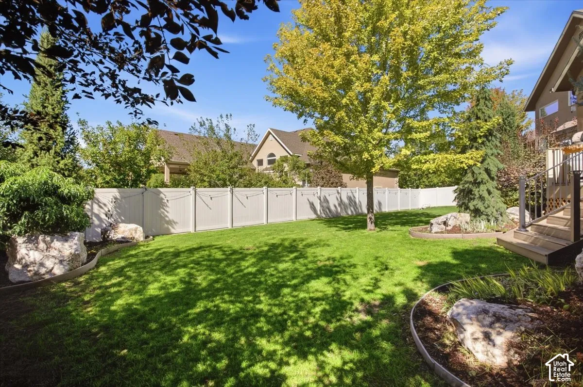 Expansive lawn area with mature trees, established landscaping beds, and a perimeter fence