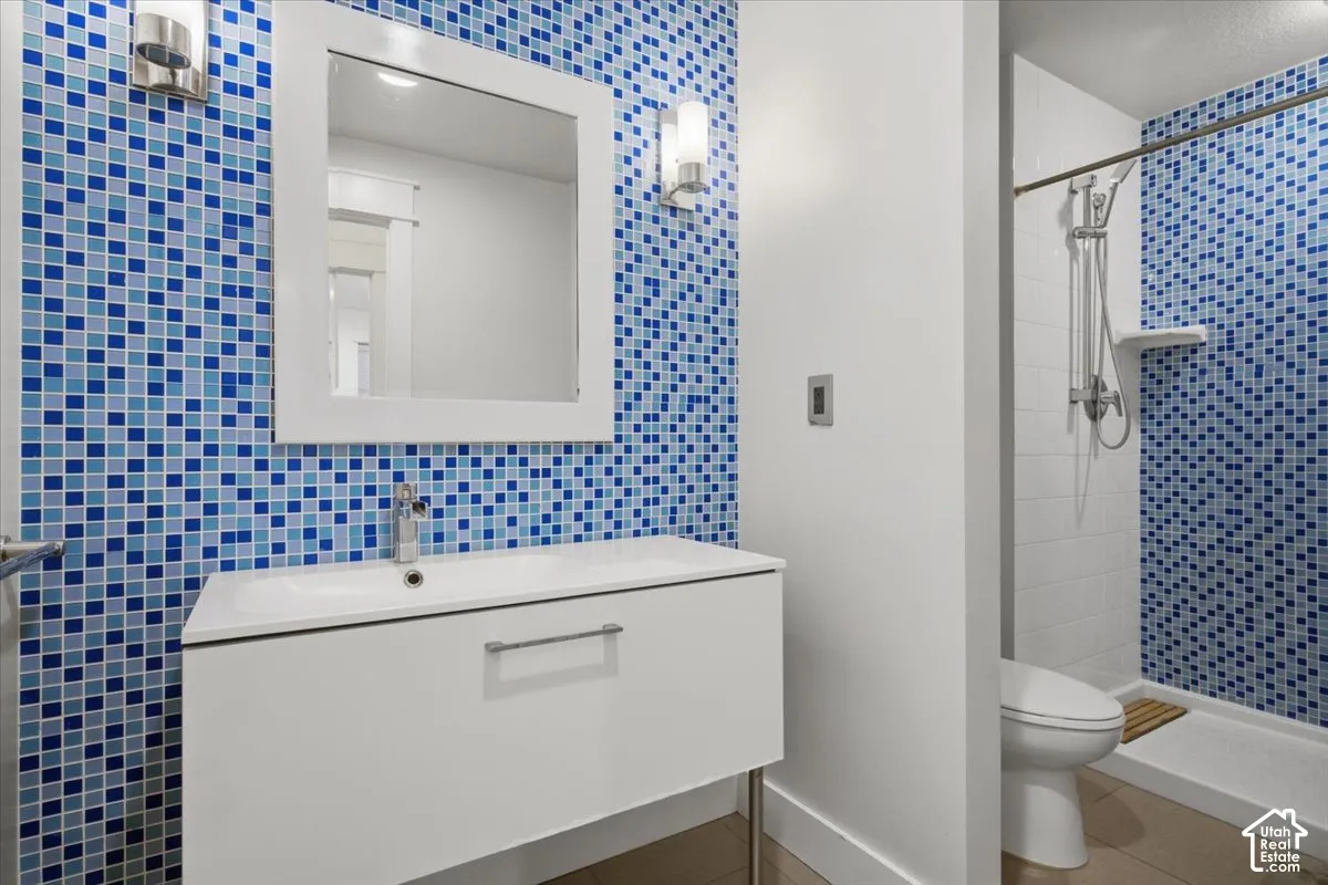 Bathroom featuring blue mosaic tile, a white vanity with an integrated sink, a framed mirror, and a shower with a built-in shelf