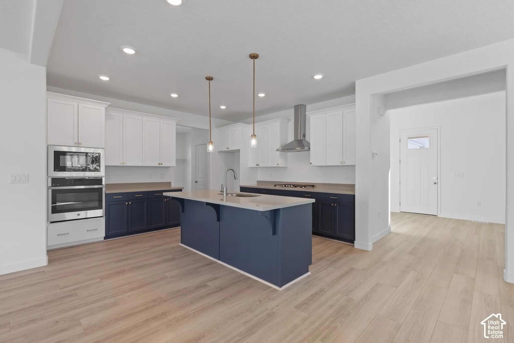 Kitchen featuring wood-finish flooring, two-tone cabinetry, a central island with sink, stainless steel appliances, and recessed lighting
