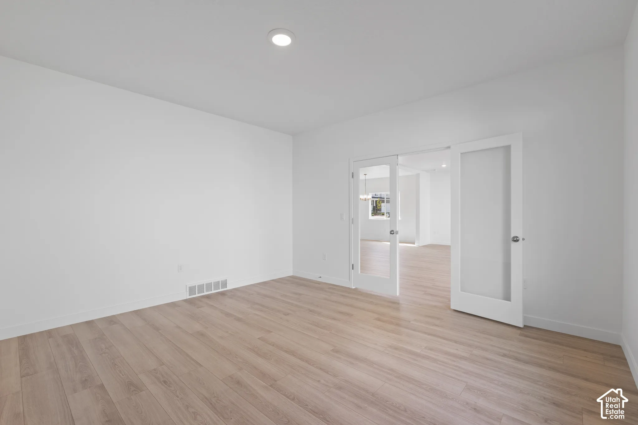 Recessed ceiling lighting, light wood-finish flooring, white walls, and double French doors with frosted glass panels