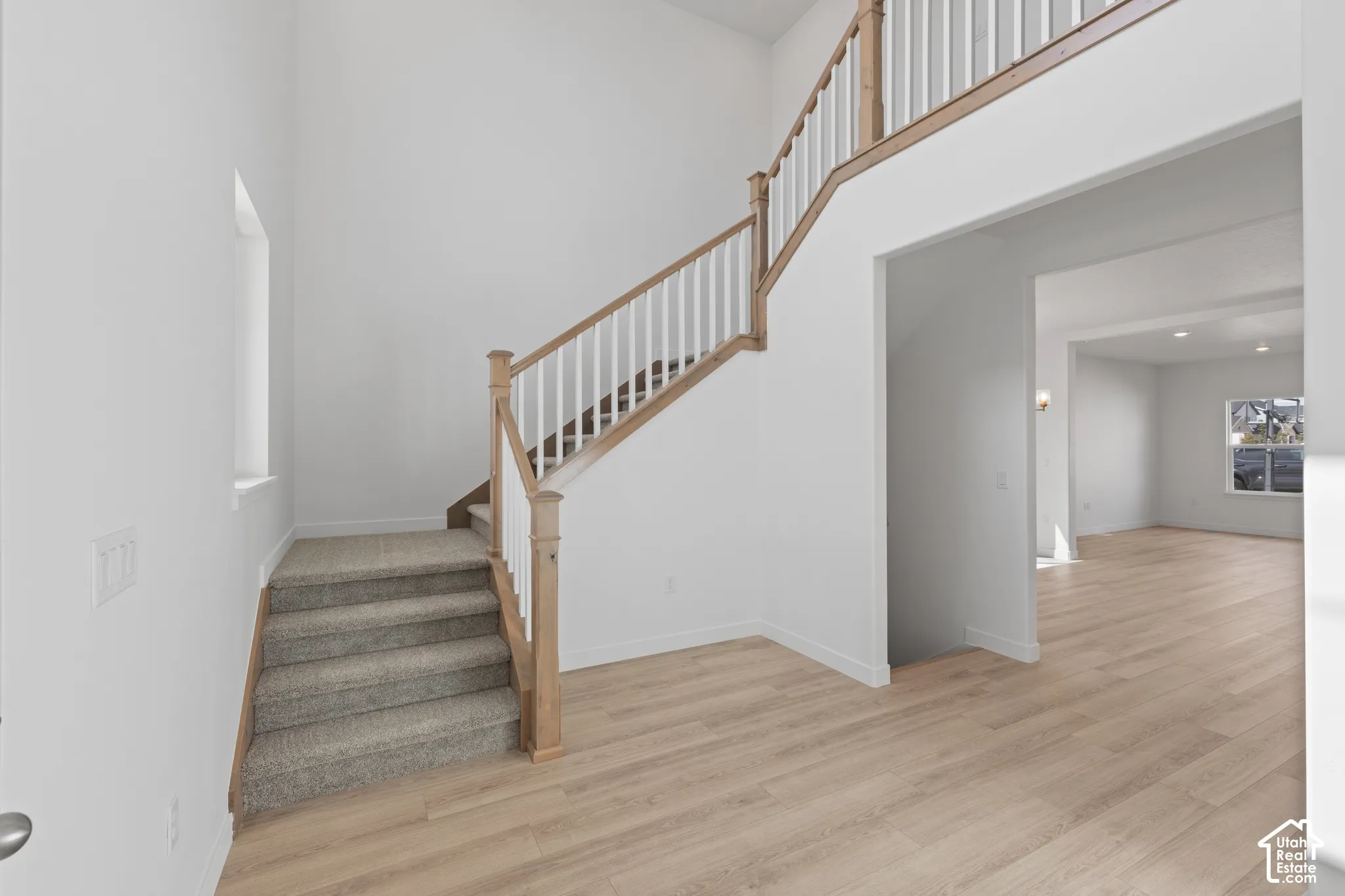 Two-story foyer with high ceilings, light wood-finish flooring, and a staircase featuring wood newel posts and handrails with white spindles