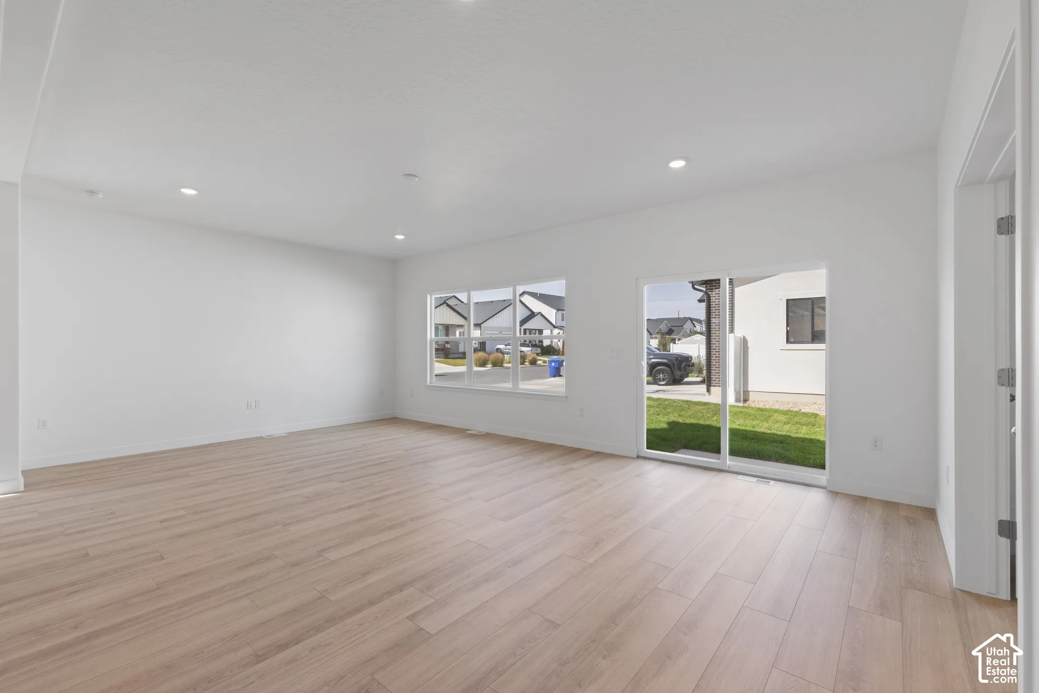Recessed lighting, light wood-finish flooring, white walls, multiple windows, and a glass sliding door to the exterior