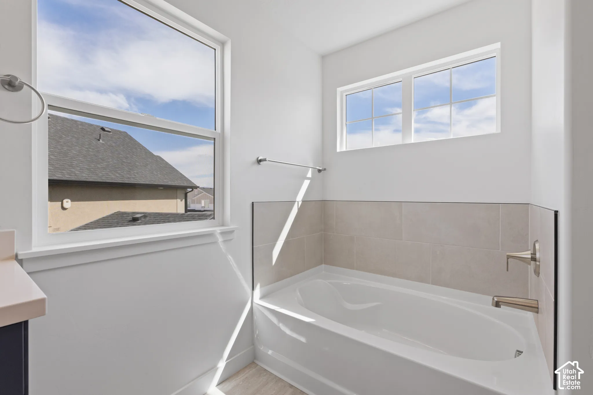 White drop-in bathtub with brushed nickel fixtures, light-toned tiled surround, and two windows