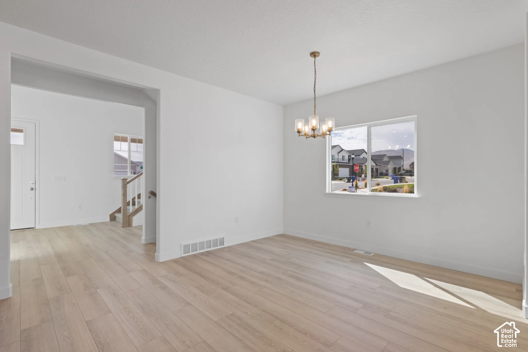 Light wood-finish flooring, white painted walls, and a modern brass chandelier with clear glass shades