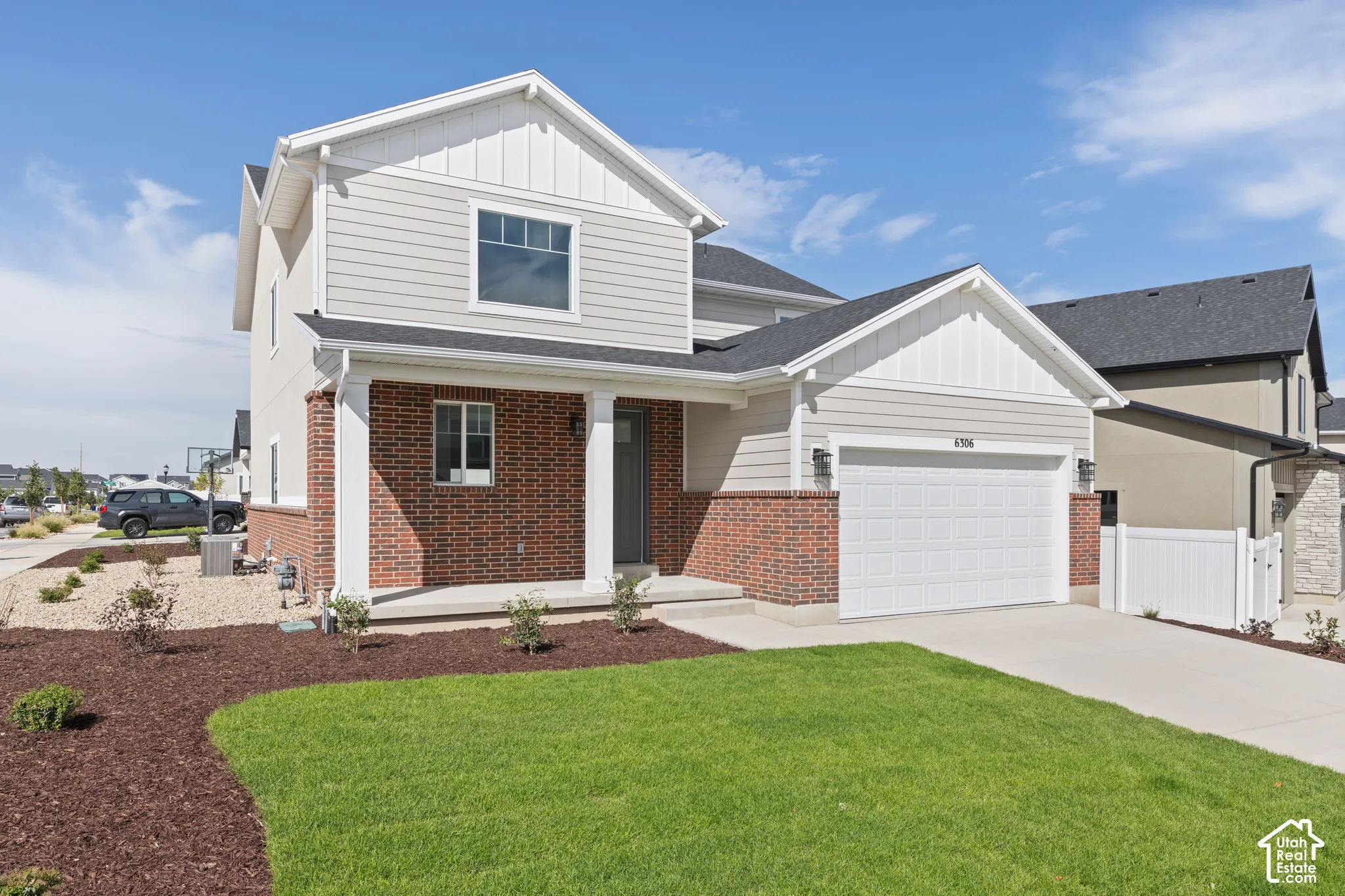 Contemporary exterior featuring a brick and siding facade, a two-car garage, a covered front porch, and a well-maintained lawn