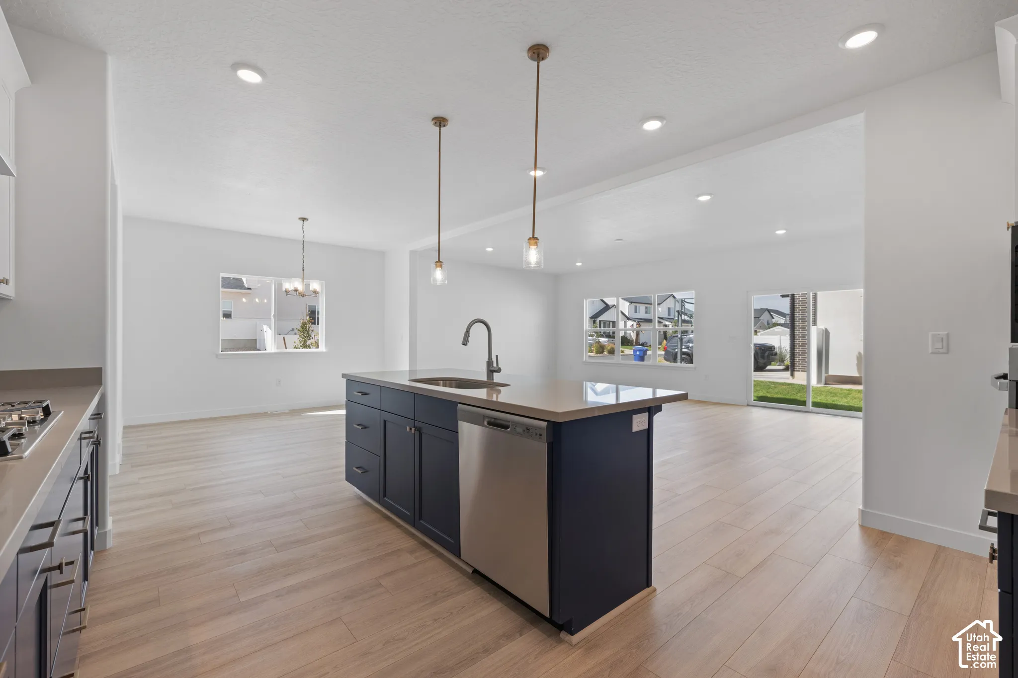 Kitchen island with integrated sink, stainless steel dishwasher, and pendant lighting