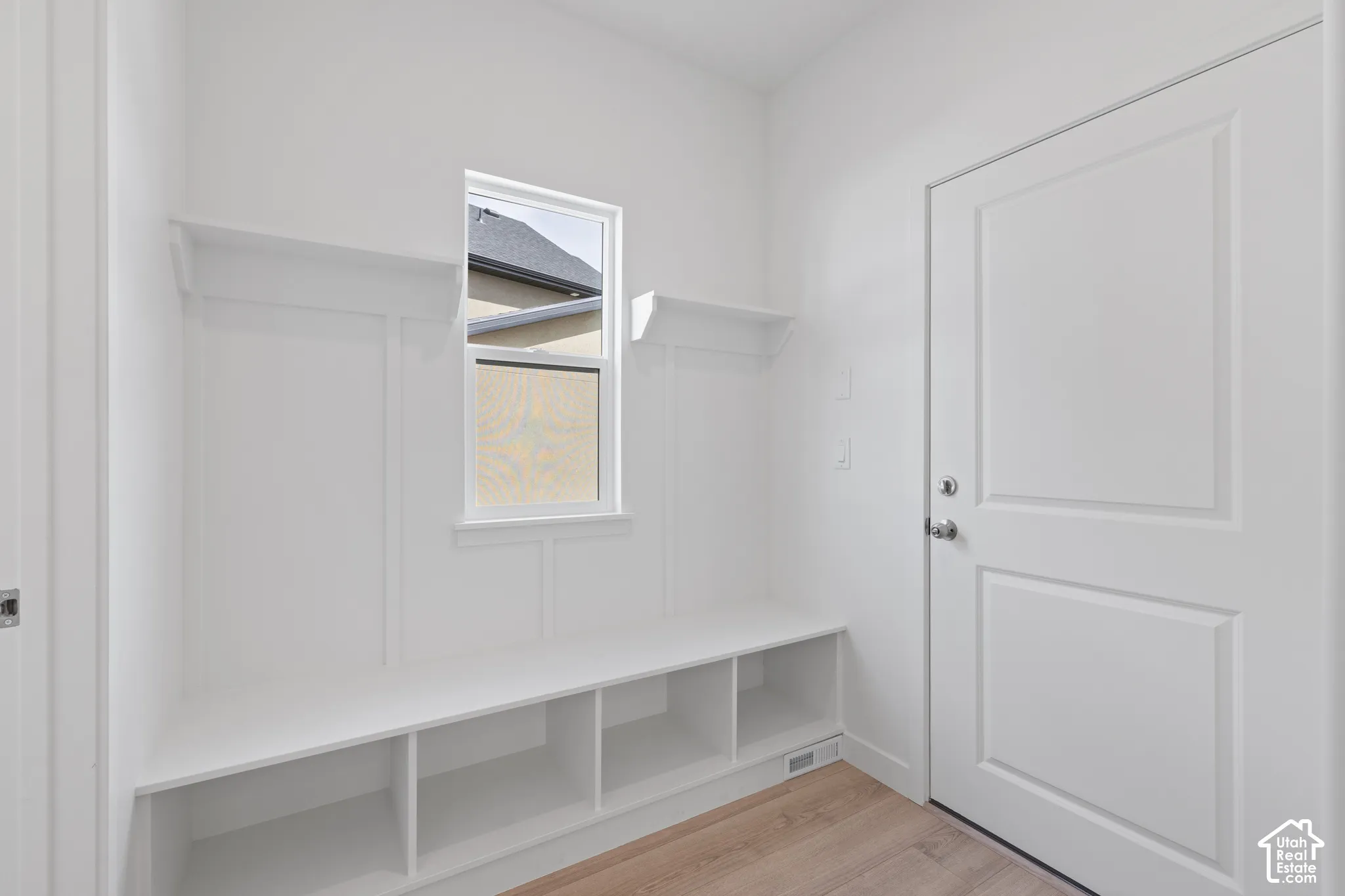 Entryway featuring a built-in bench with cubbies, upper shelving, paneled accent wall, and wood-finish flooring