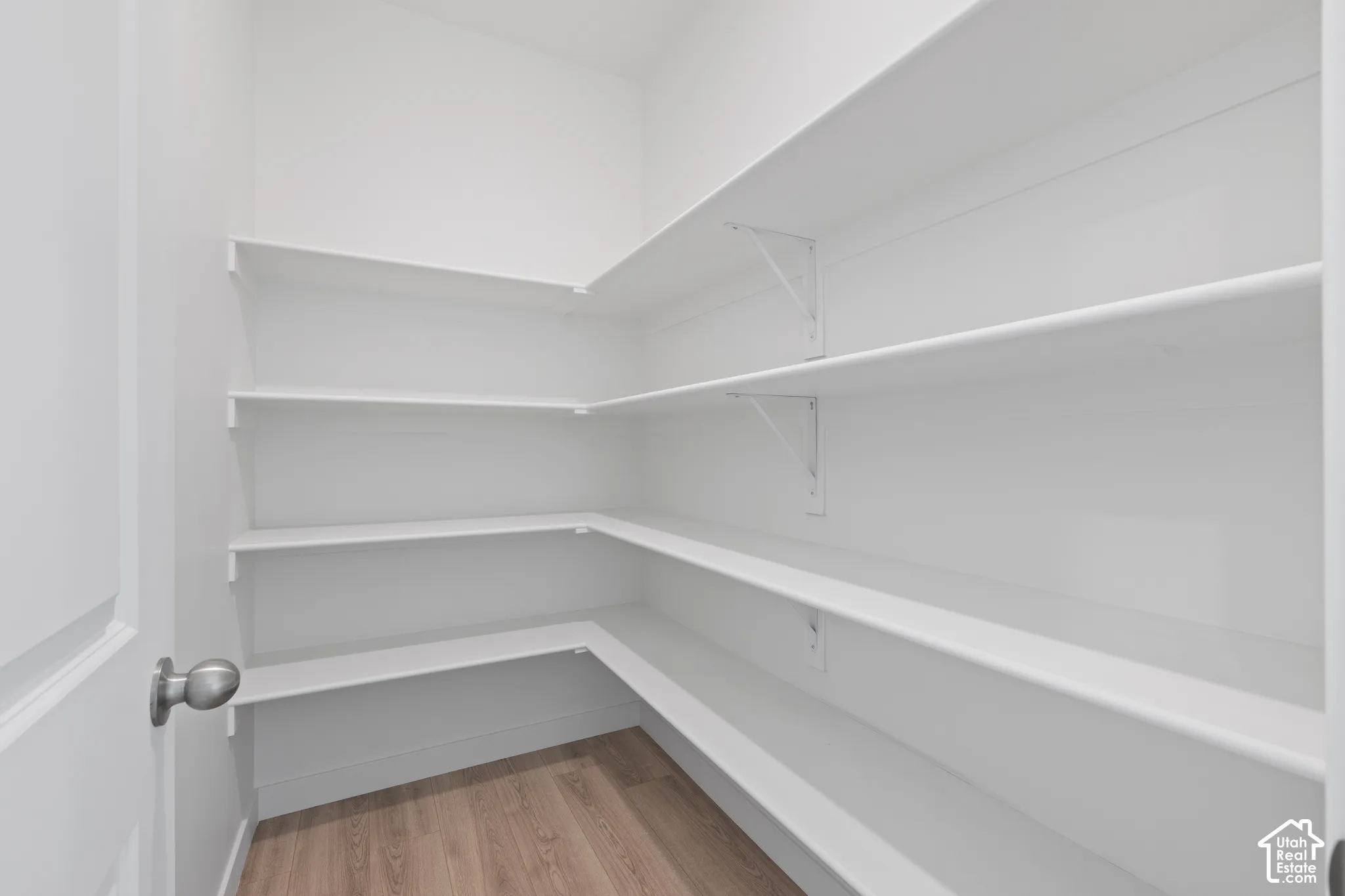 Walk-in pantry featuring multiple levels of white shelving, corner shelving units, and wood-finish flooring