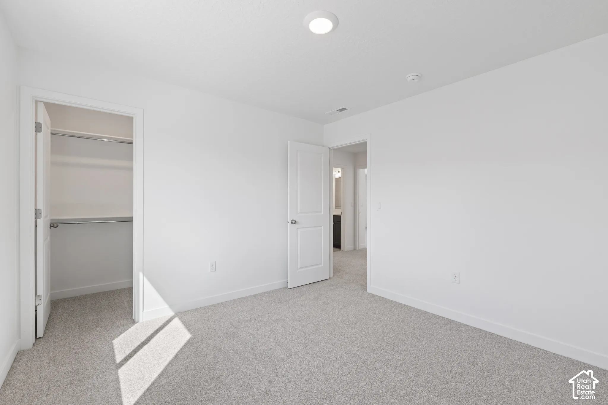 Plush carpet flooring, white painted walls, recessed ceiling light, and a closet with shelving and hanging rods
