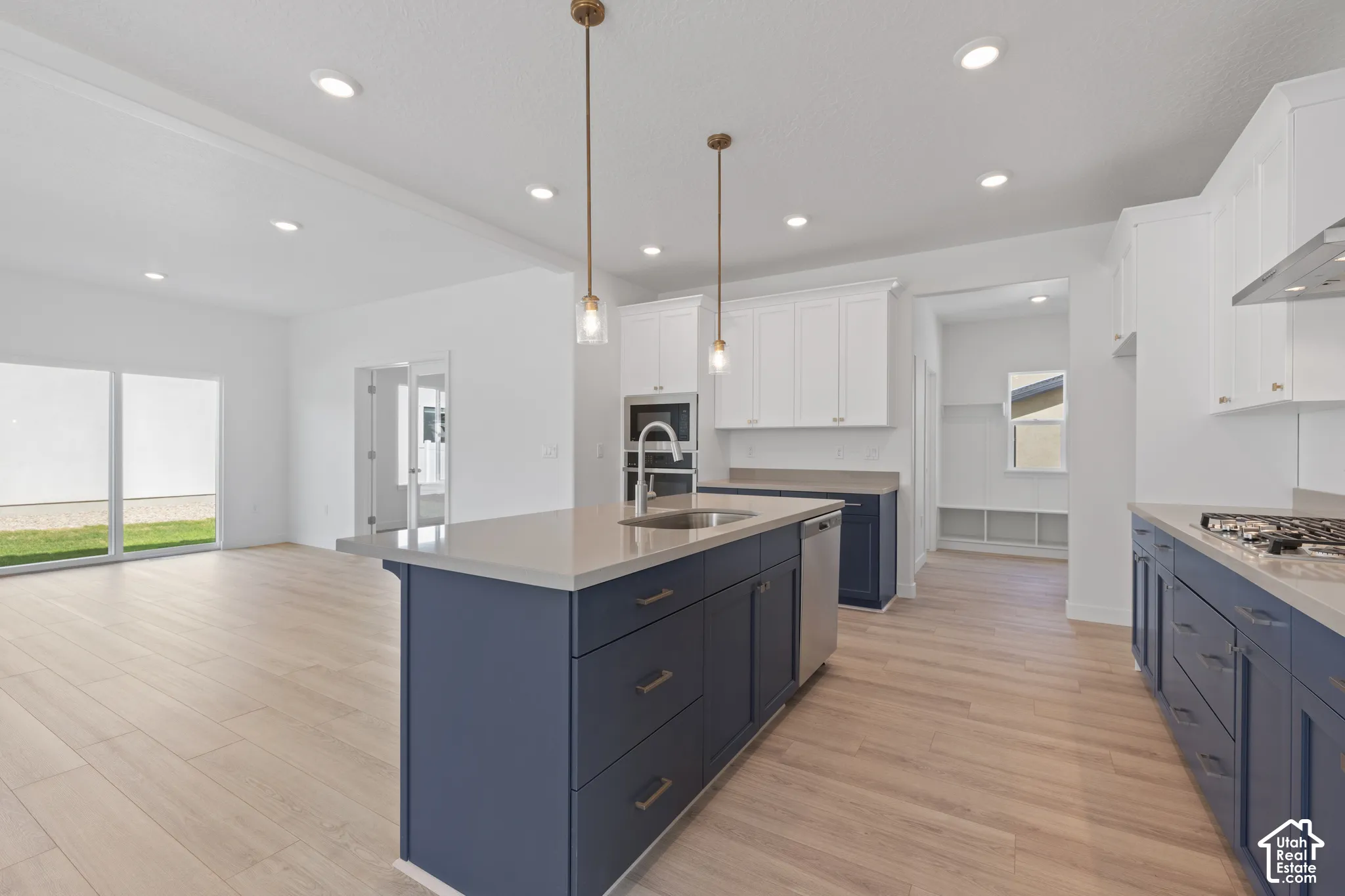 Modern kitchen featuring a central island with a built-in sink and pendant lighting, wood-finish flooring, white upper cabinetry, and dark blue lower cabinetry