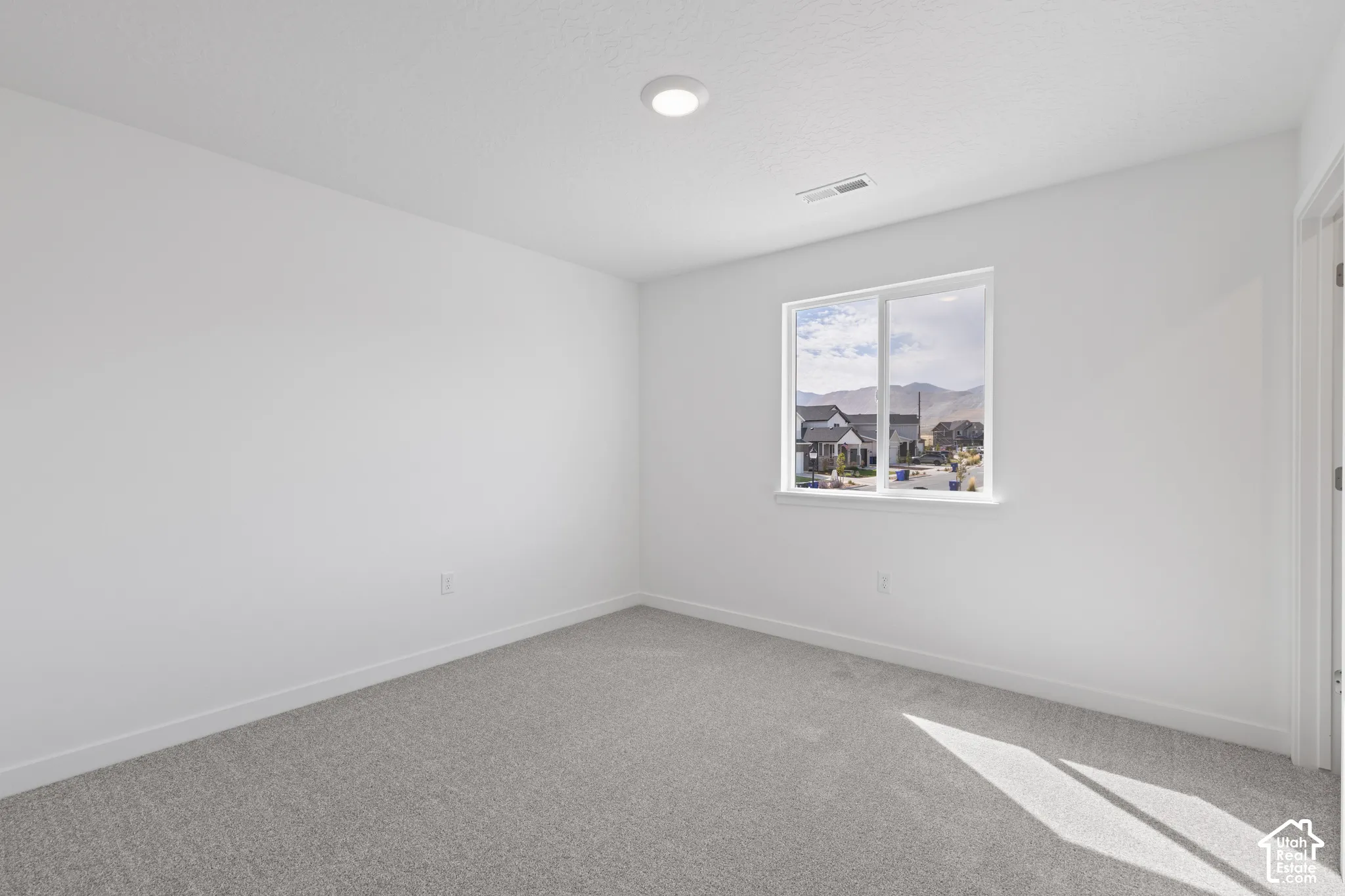 Neutral wall color, light gray carpeting, recessed ceiling lighting, and a single window