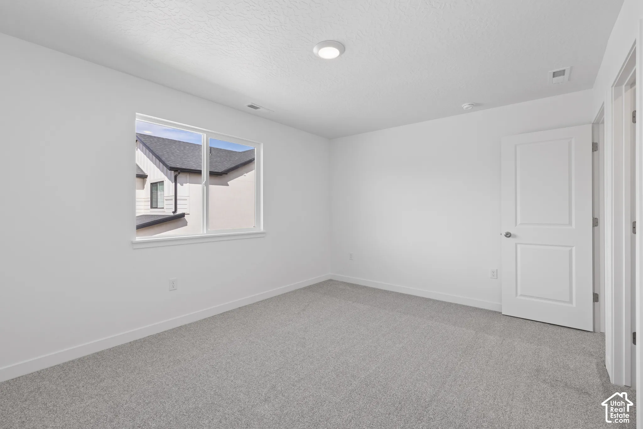 Neutral color palette, window with white trim, gray carpeting, white walls, flush mount lighting
