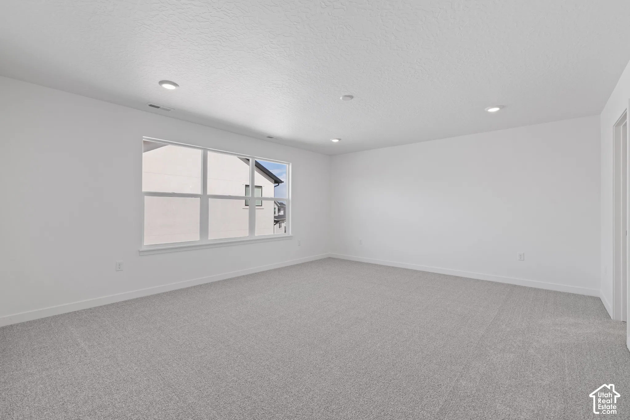 Recessed lighting illuminates this room featuring light gray carpeting and a multi-pane window
