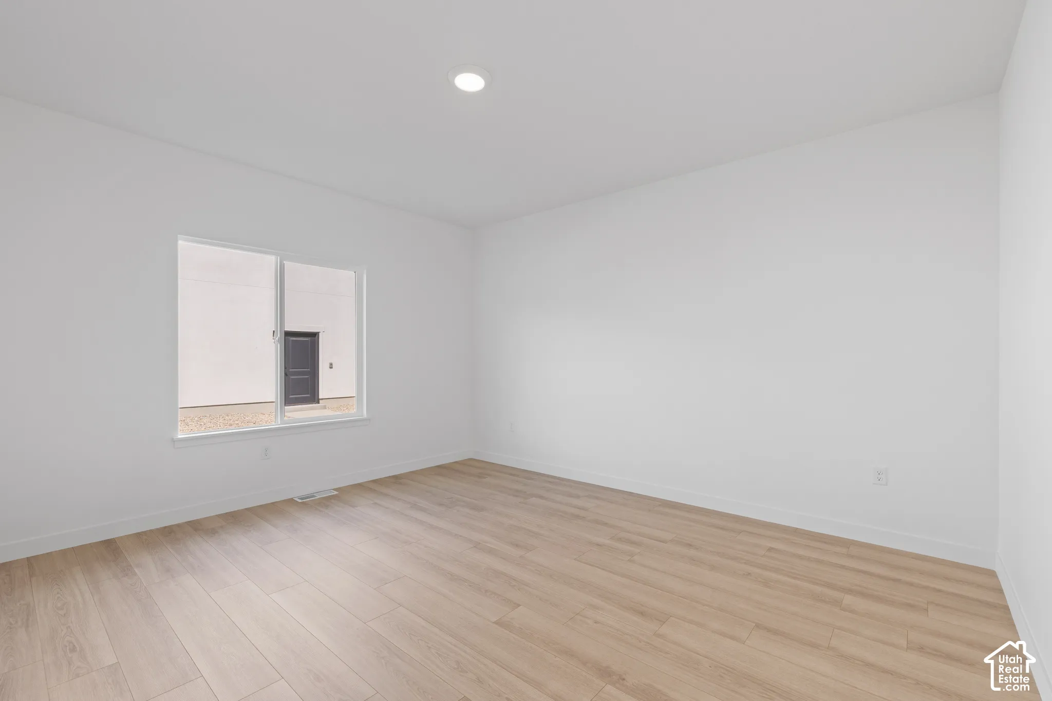 Room featuring light wood-finish flooring, white walls, and a single recessed ceiling light fixture