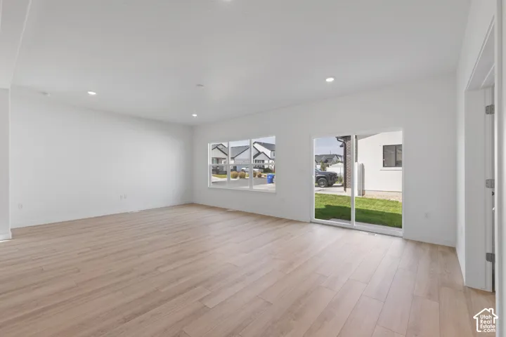 Recessed lighting, light wood-finish flooring, white walls, multiple windows, and a glass sliding door to the exterior