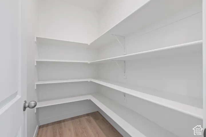 Walk-in pantry featuring multiple levels of white shelving, corner shelving units, and wood-finish flooring
