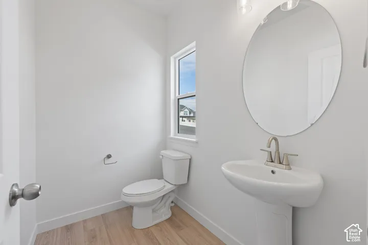 Pedestal sink with brushed nickel faucet, oval mirror, wall-mounted light fixture, and wood-finish flooring