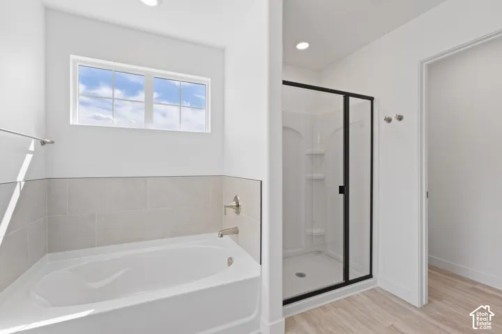 White soaking tub, light-toned wall tile, transom window, separate shower with black-framed glass enclosure, and wood-finish flooring