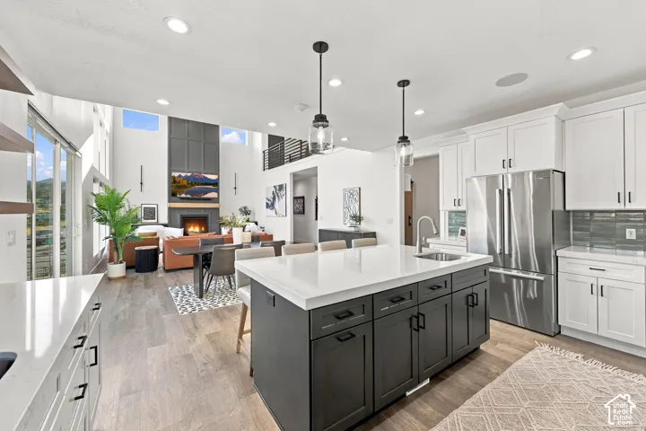 Open-concept interior featuring a two-story great room with a fireplace, a kitchen island with seating, a stainless steel refrigerator, and wood-finish flooring throughout