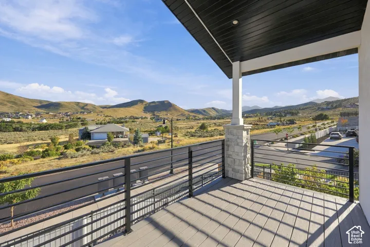 Balcony with wood-finish decking, black horizontal railings, stone-clad pillar, and an overhead soffit